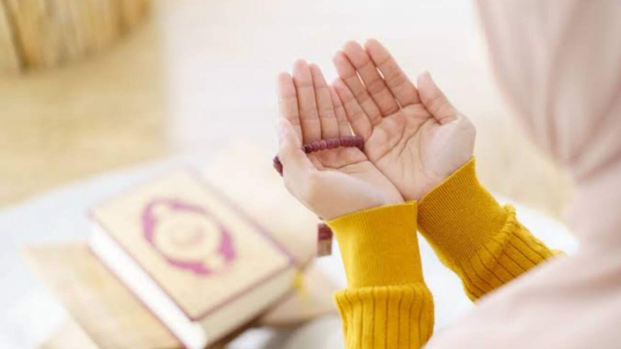Seorang wanita muslim sedang berdoa dengan khusyuk sambil memegang Al-Qur'an, menggambarkan salah satu adab agar doa terkabul